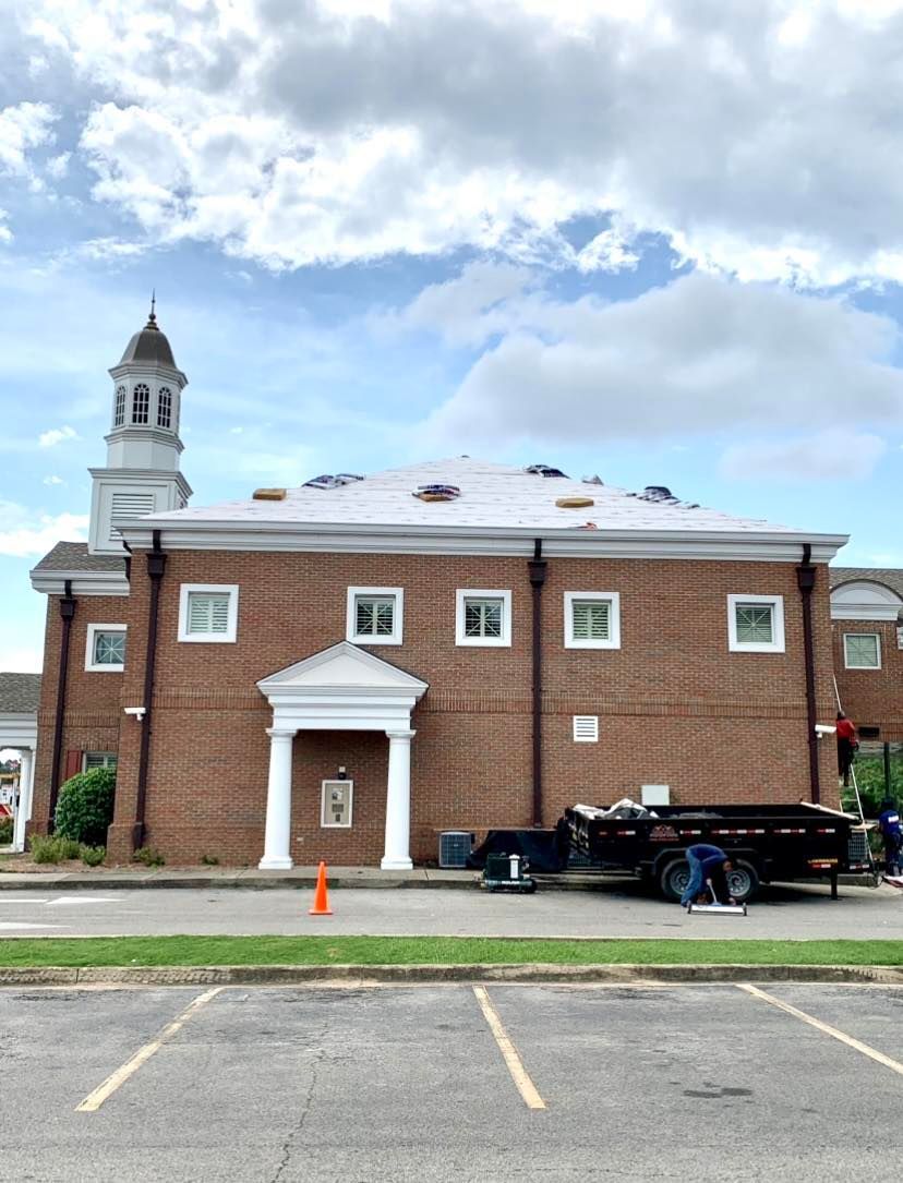 A brick building with a white cupola and a white entrance portico under repair, with a dumpster trailer in the parking lot.