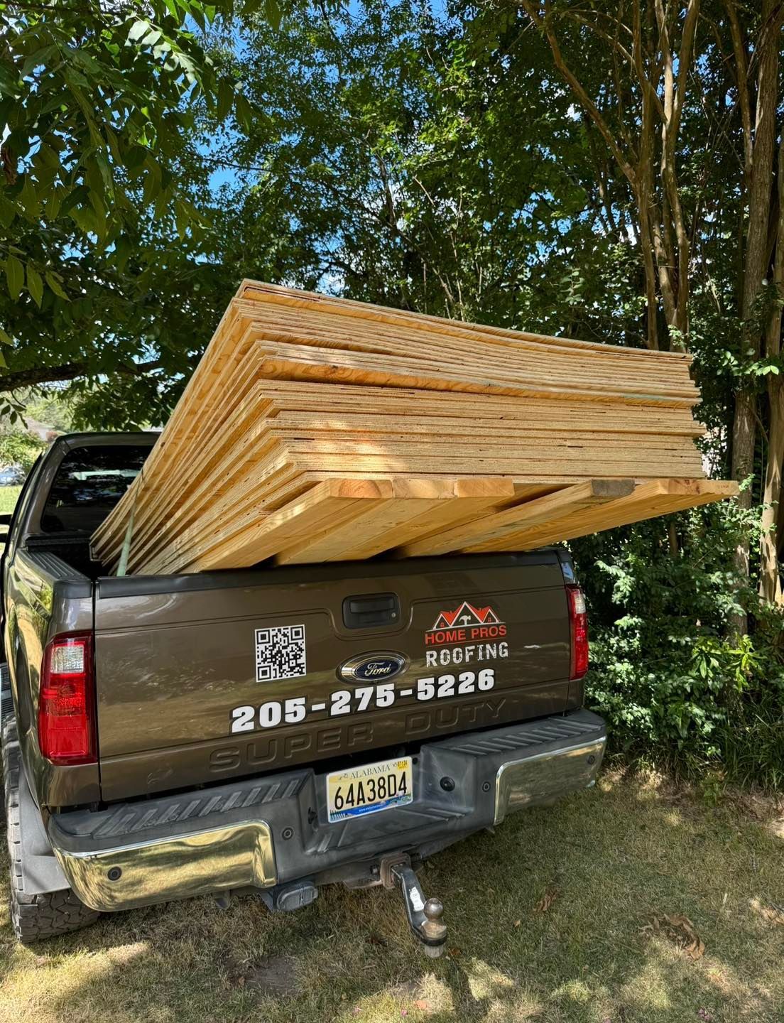 A dark brown Ford pickup truck parked outdoors, loaded with a large stack of plywood sheets protruding from the tailgate.