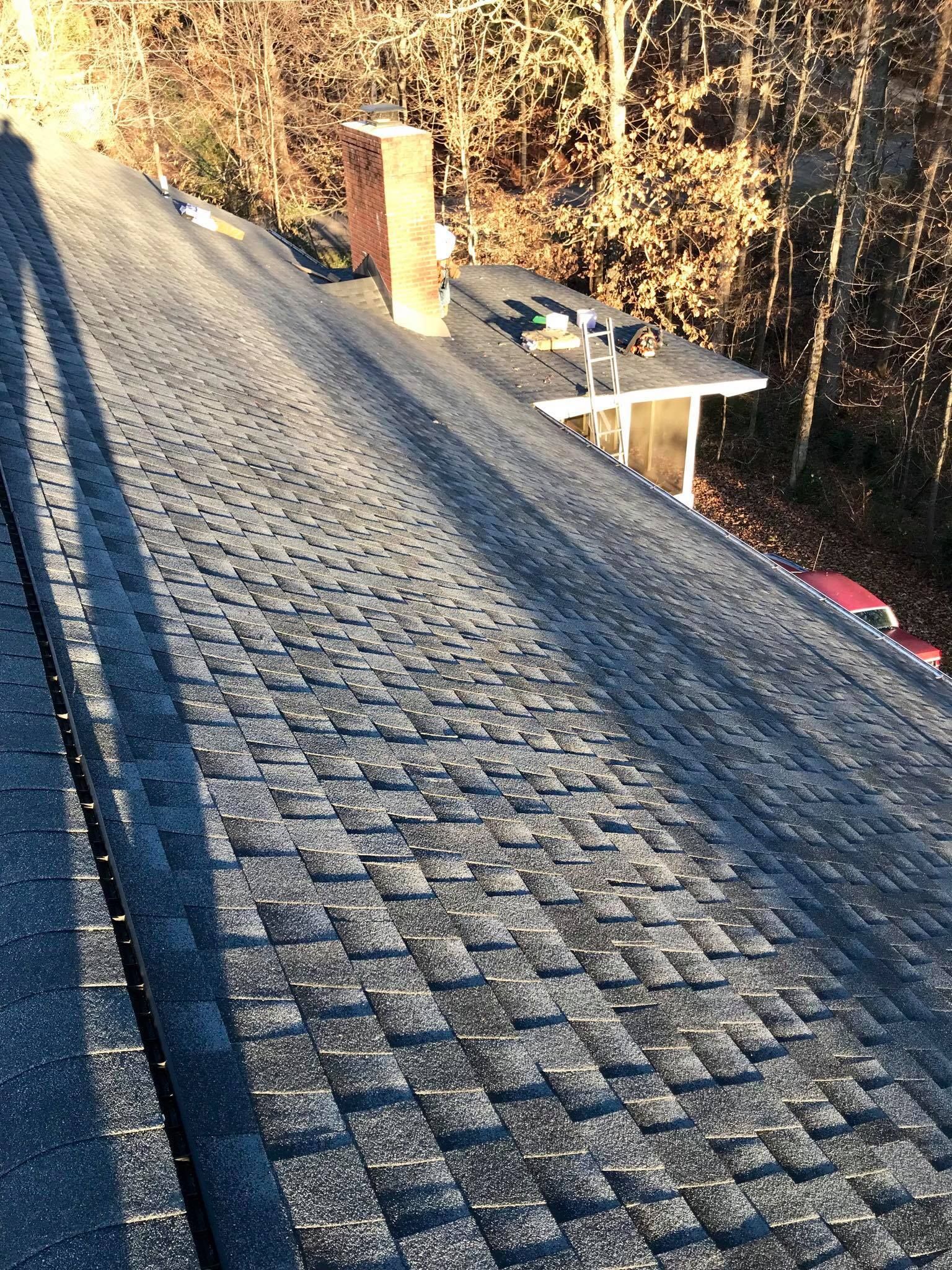 A high-angle view looking down a residential roof with grey textured shingles and a brick chimney.