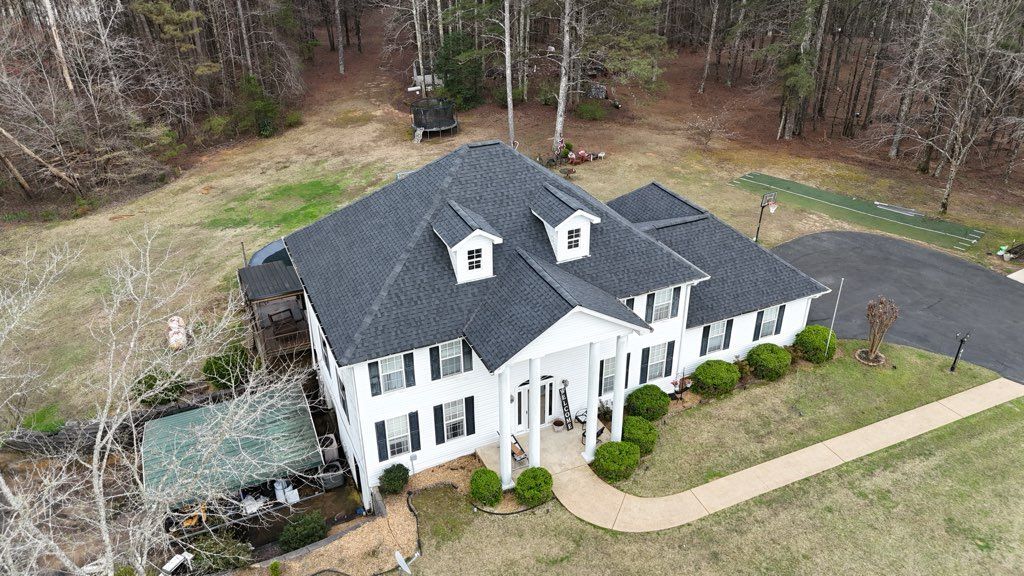 Aerial view of a large white house with a dark roof, driveway, and trees around it