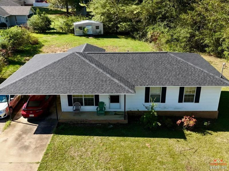 Aerial view of a white single-story house with a grey roof, a porch, and a car parked in the driveway.