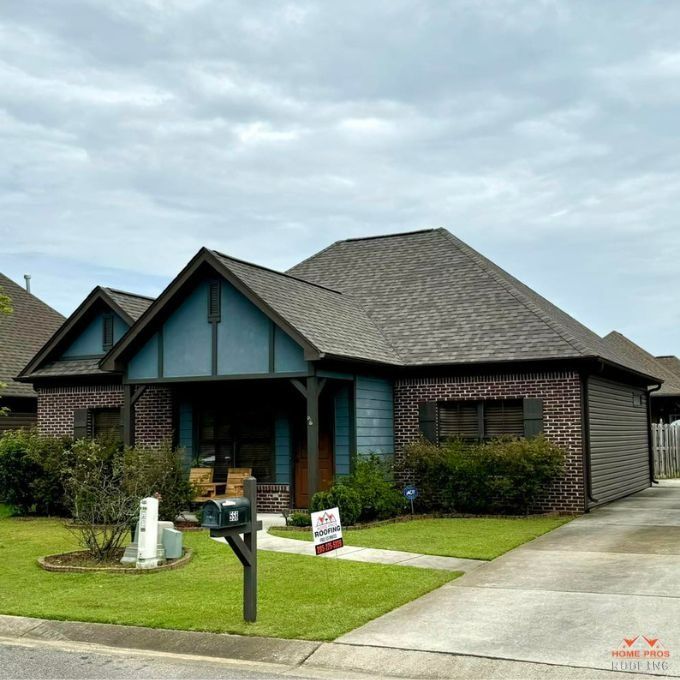 A single-story house with dark brick, blue gable accents, a shingled roof, a front porch, and a concrete driveway.