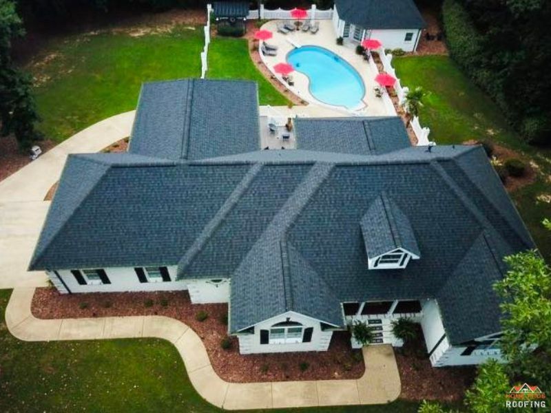 Aerial view of a white home with a dark gray shingled roof, a curved walkway, and a backyard pool with red umbrellas.