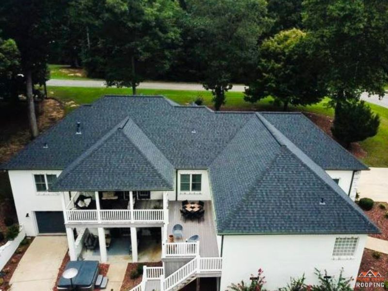 An aerial view of a white two-story house with a dark shingled roof, featuring a back patio, deck, and hot tub.