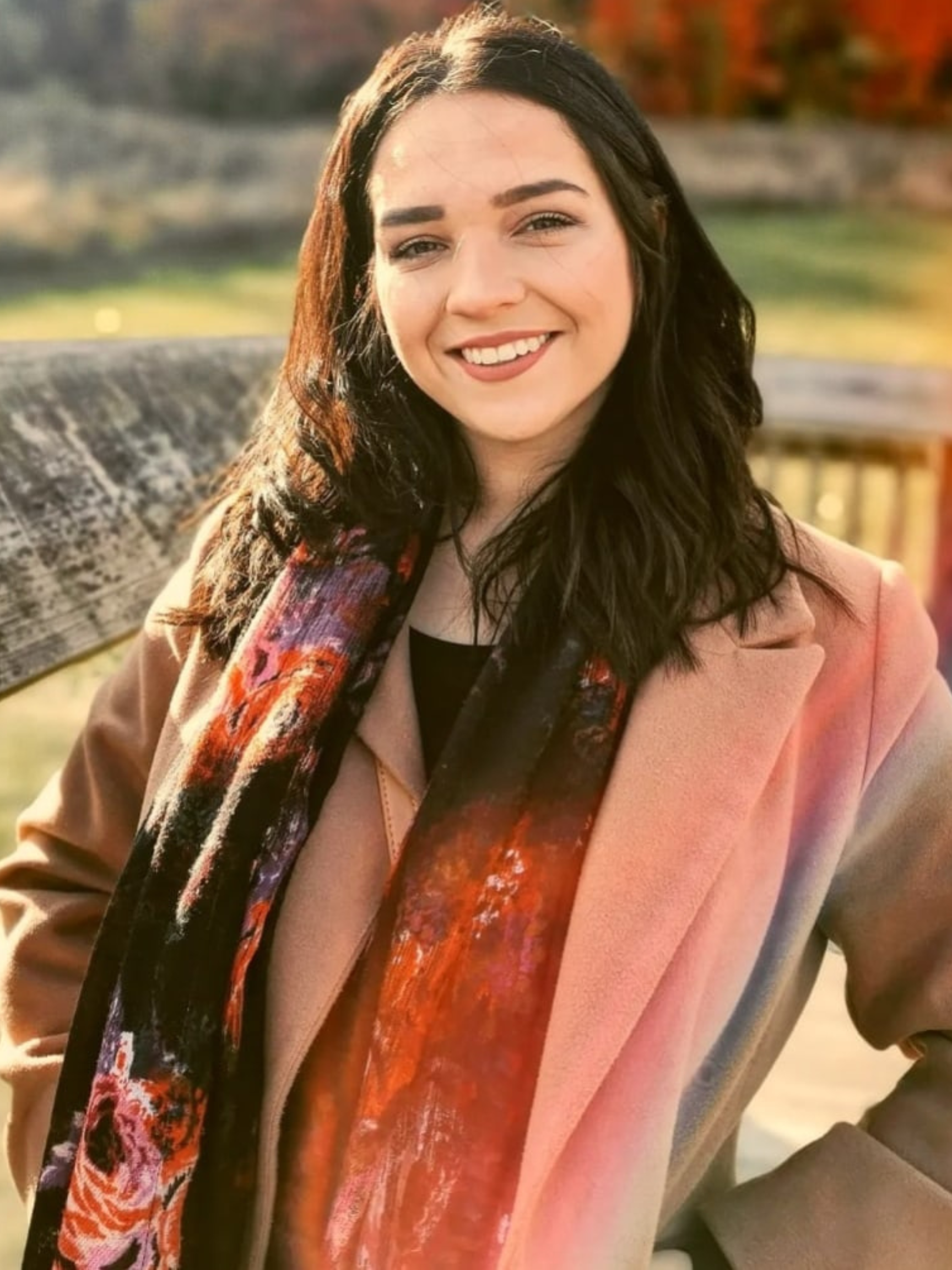 A woman wearing a scarf and a coat is smiling for the camera.