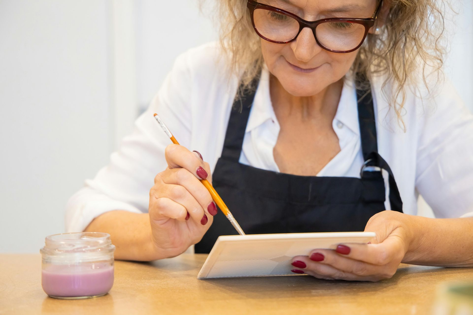 A woman is sitting at a table painting a picture with a brush.