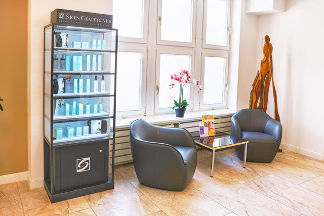 Ein Wartebereich eines Schönheitssalons mit Produktvitrine, Sesseln, Tisch und Fenster mit Blumen.
