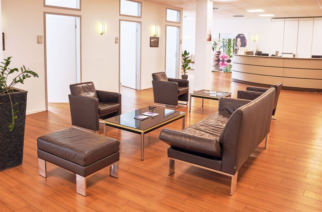 Wartezimmer mit Ledermöbeln, Couchtischen, Pflanzen und Empfangstresen.