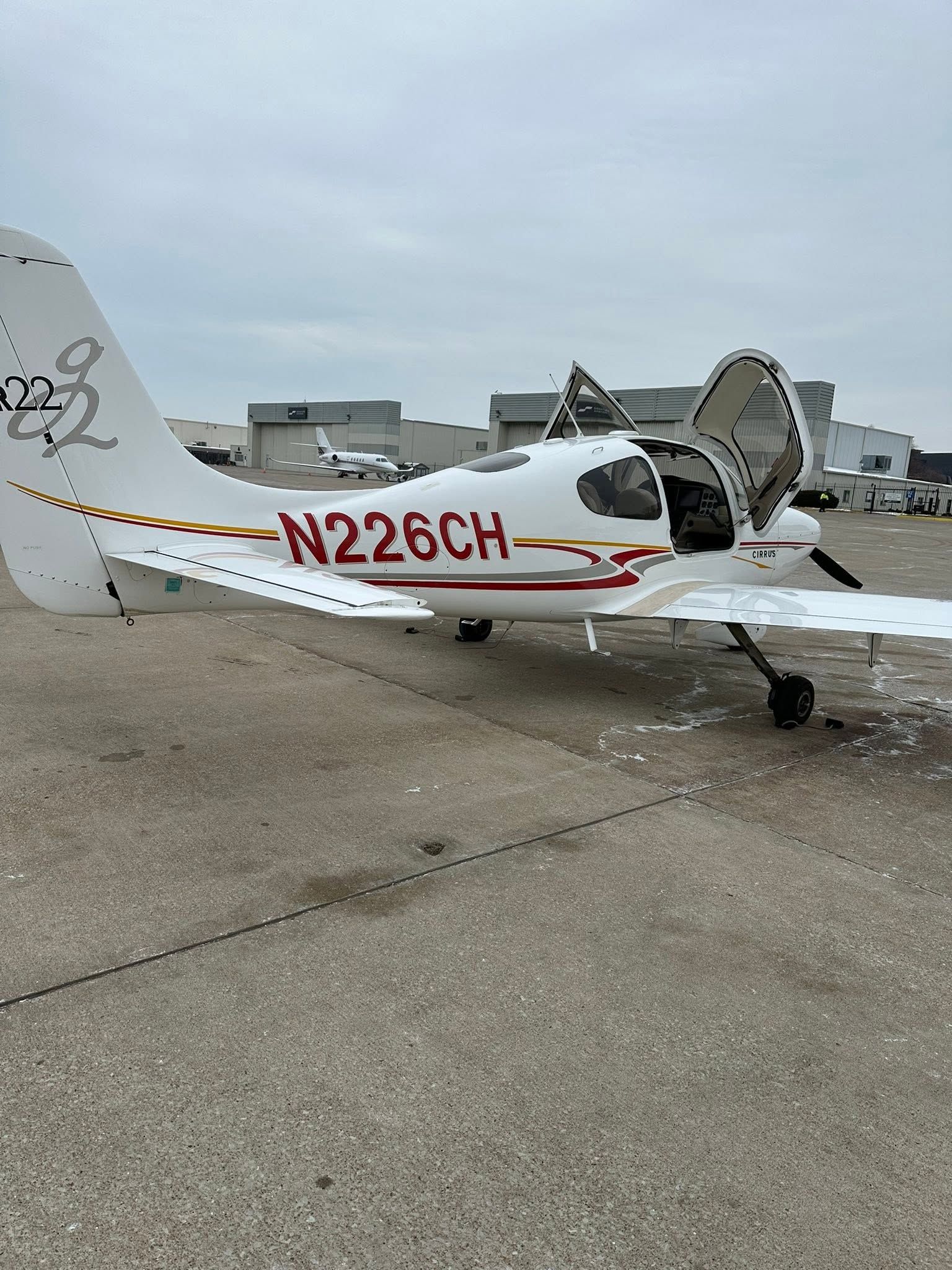 Small white single-engine airplane with red registration N226CH parked on a tarmac under a cloudy sky