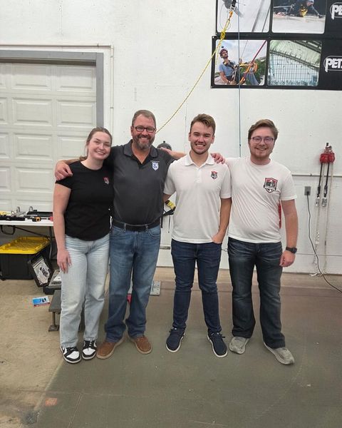 Four people standing together in a workshop, smiling at the camera.