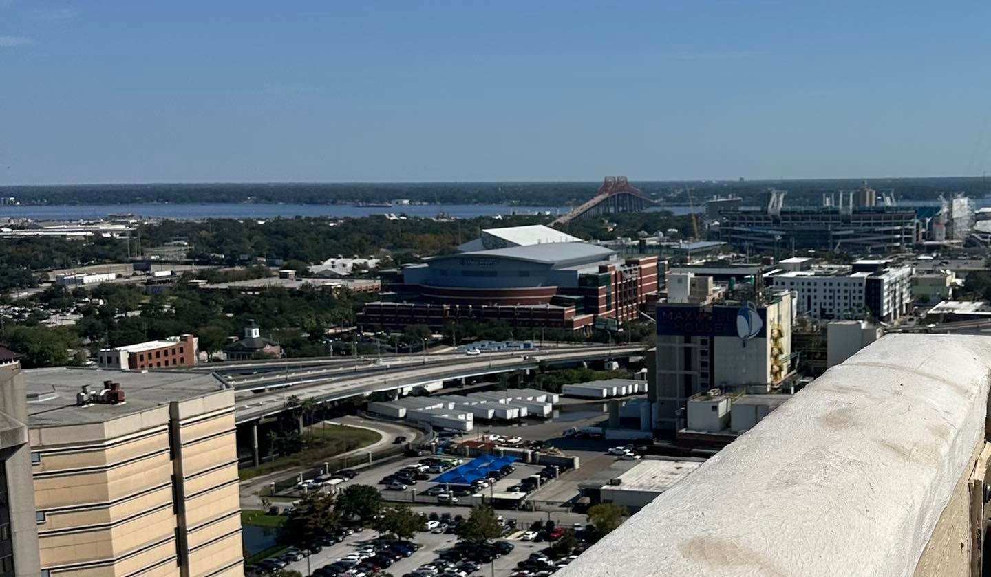 City skyline with waterfront, buildings, roads, and a distant stadium under a clear blue sky
