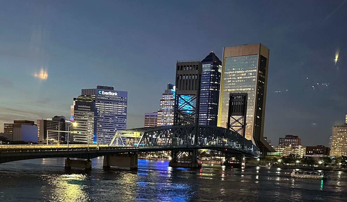 City skyline at dusk with a lit bridge over water and reflections from illuminated office towers