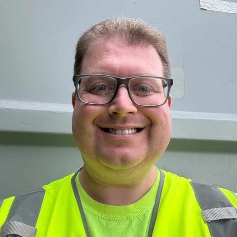 Smiling person in glasses wearing a neon yellow safety shirt and reflective vest
