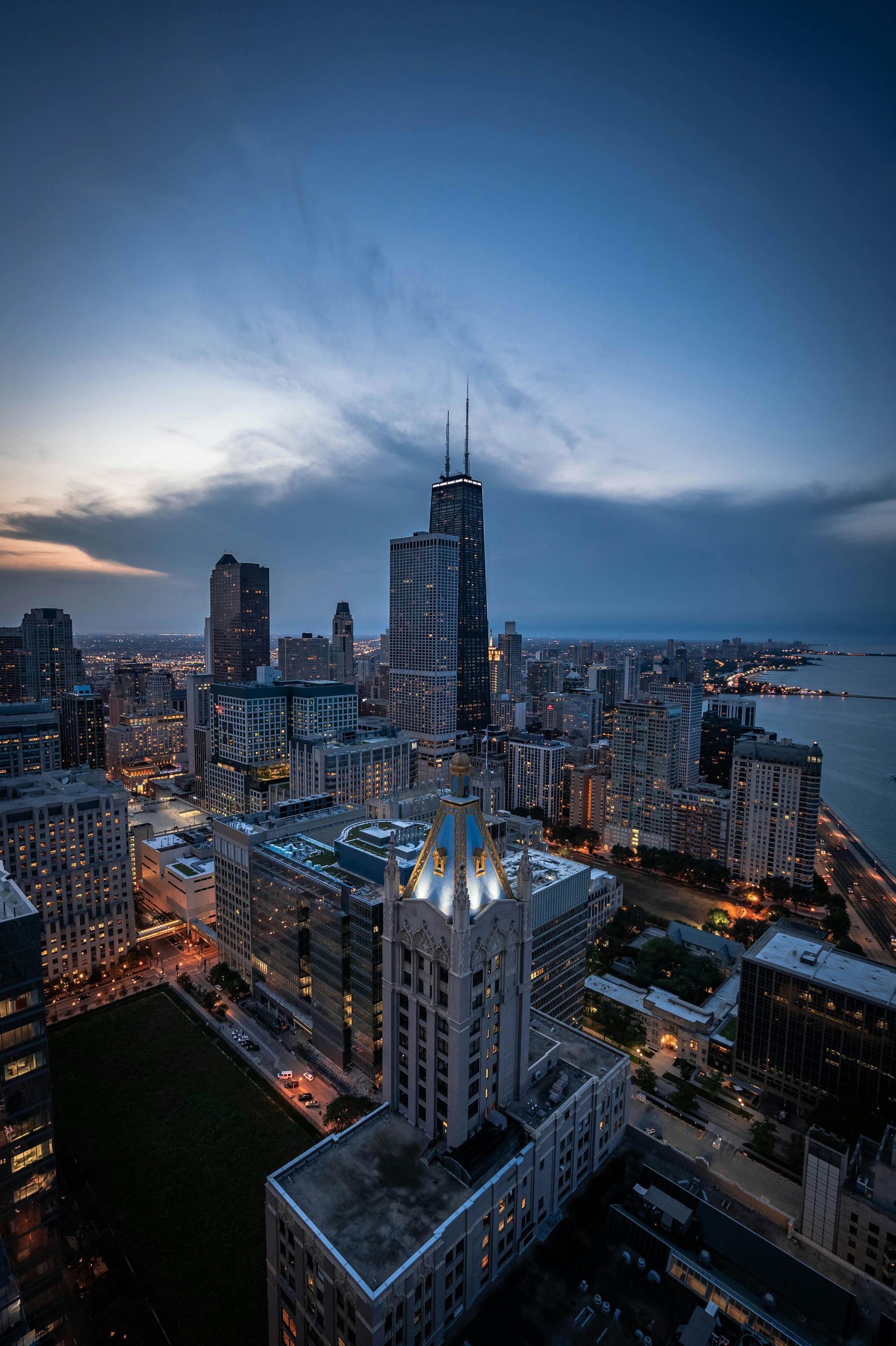 Dusk city skyline with illuminated skyscrapers and a waterfront under a blue evening sky