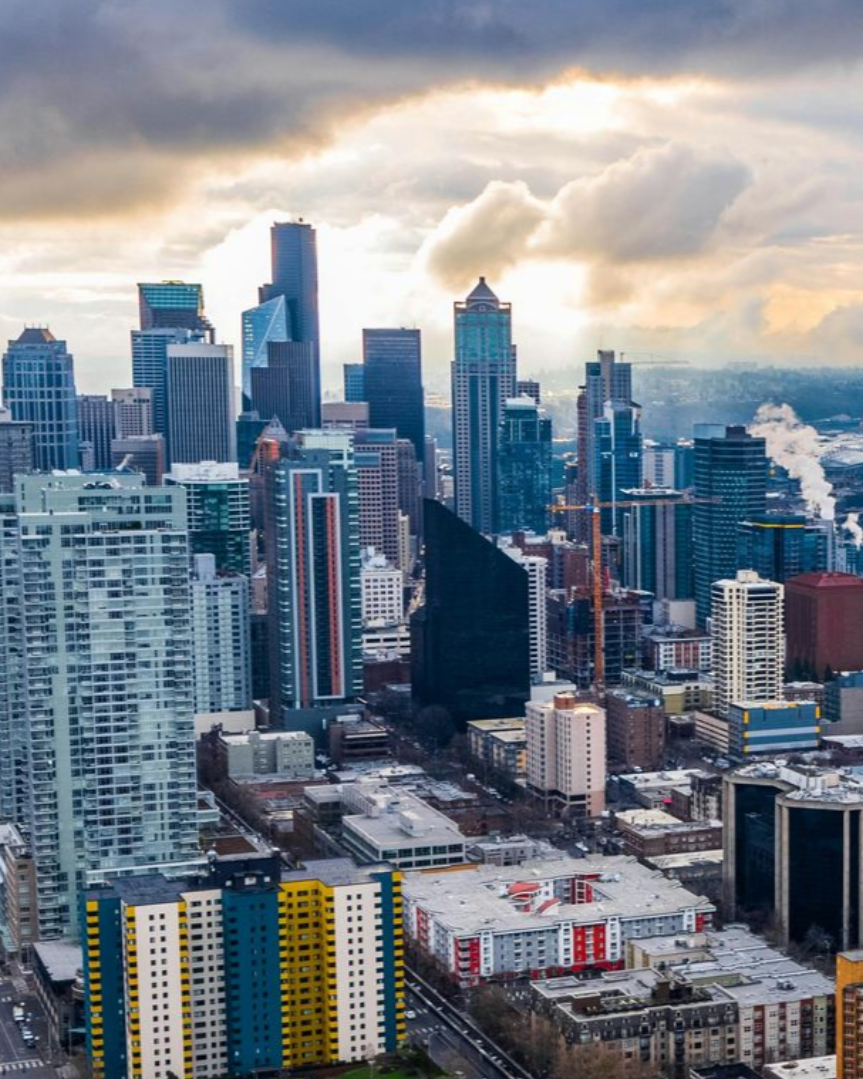 City skyline with tall modern buildings under a cloudy, dramatic sky