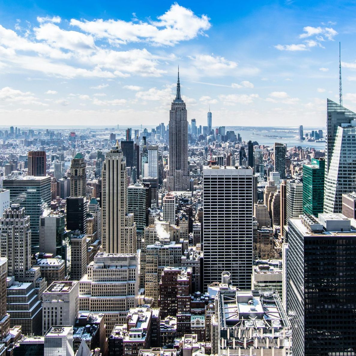 Skyline of Manhattan with the Empire State Building under a bright blue sky and clouds