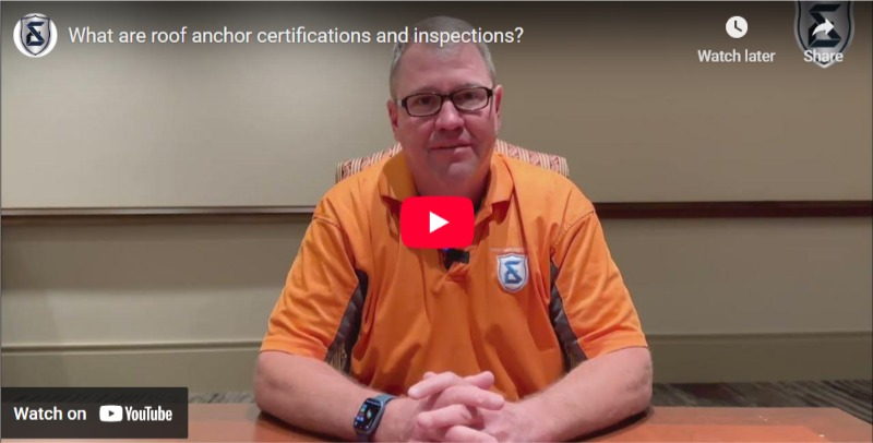 Man seated at a table in an orange shirt, shown in a paused YouTube video about roof anchor certifications.