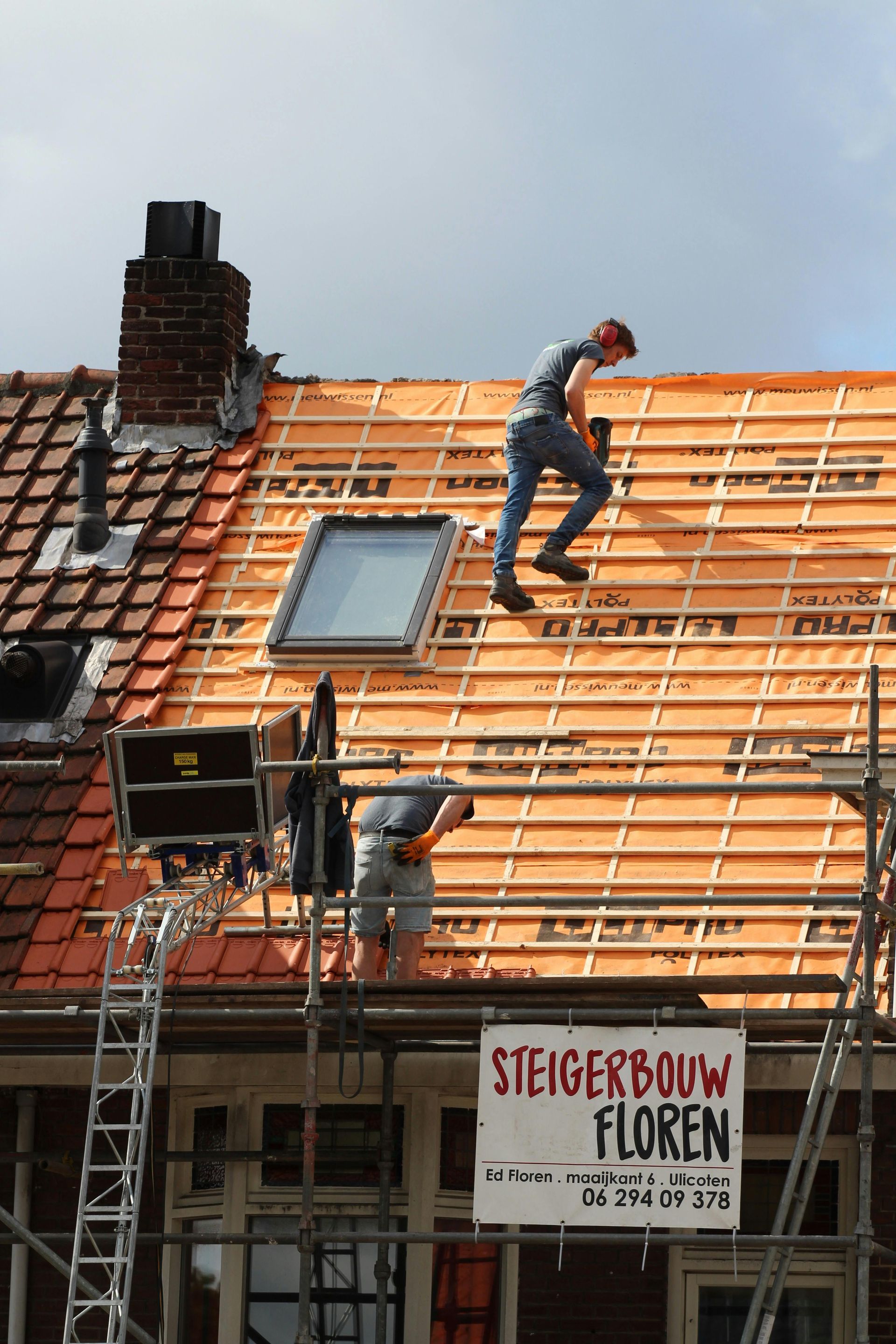 A man is standing on top of a roof with a sign that says steigerbouw floren