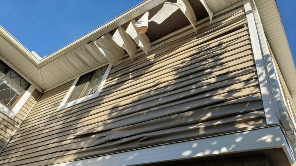 Looking up at the side of a house which is damaged and a blue sky in the background.