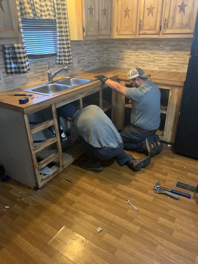 Two men are working under a sink in a kitchen.