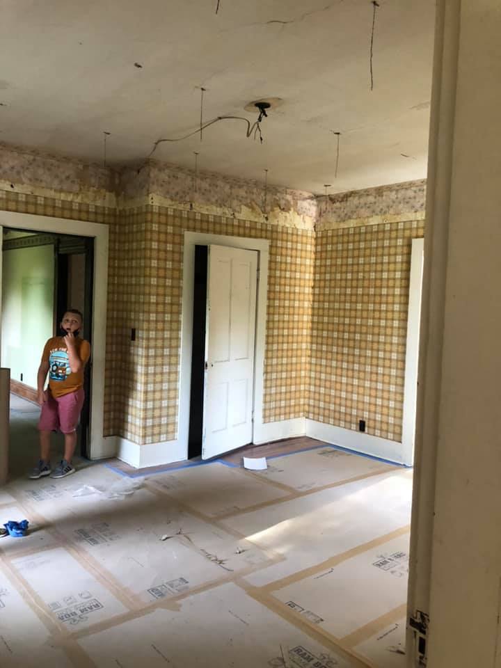 A girl is standing in an empty room with yellow plaid wallpaper.