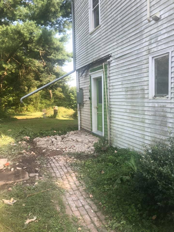 A white farmhouse with a green door and a brick walkway leading to it.