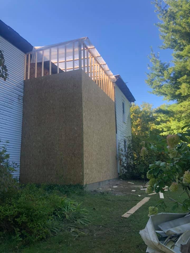 A large wall is being built on the side of a white farmhouse.