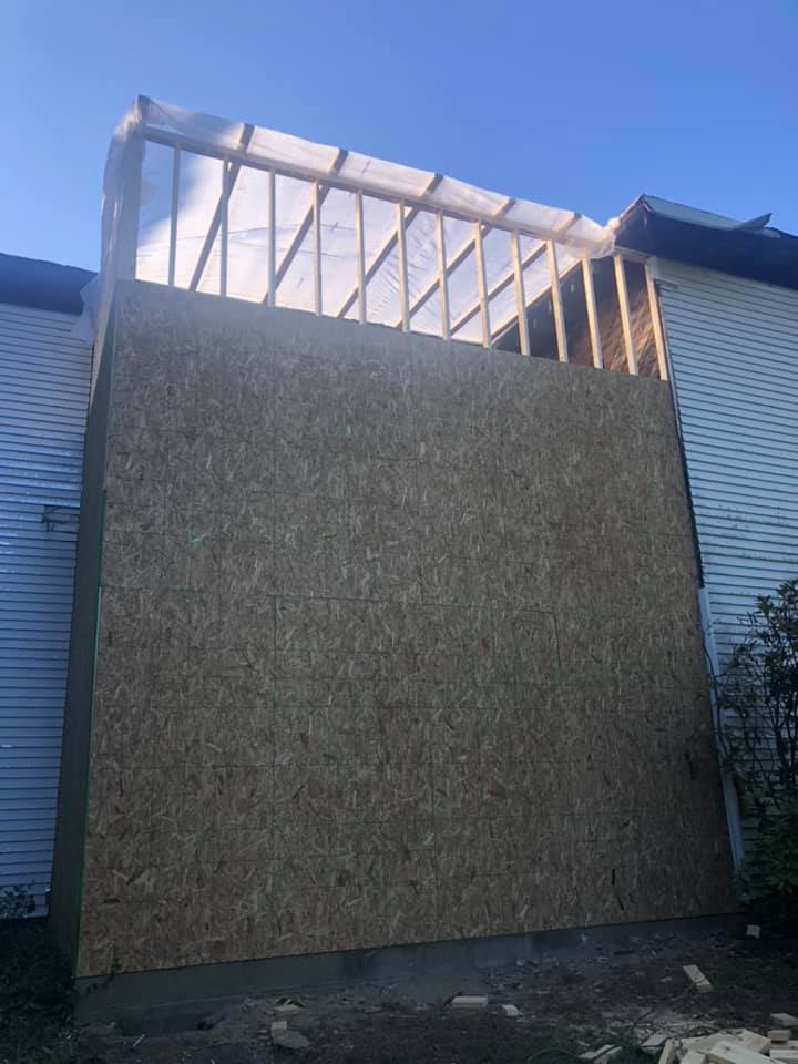 A large wall is being built on the side of a white farmhouse.