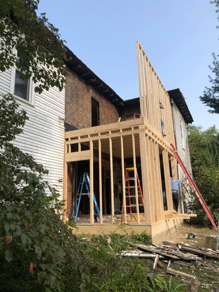 A white house is being remodeled with a red ladder on the side and two ladders inside.