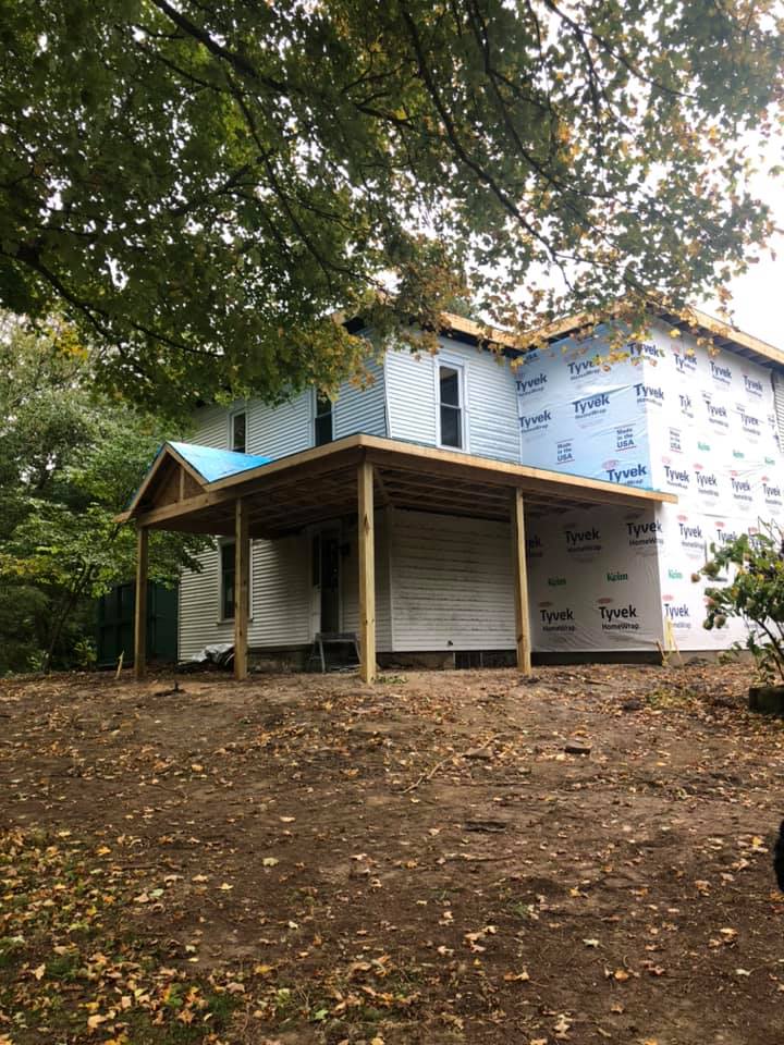 A farmhouse with a porch and a blue roof is being remodeled.