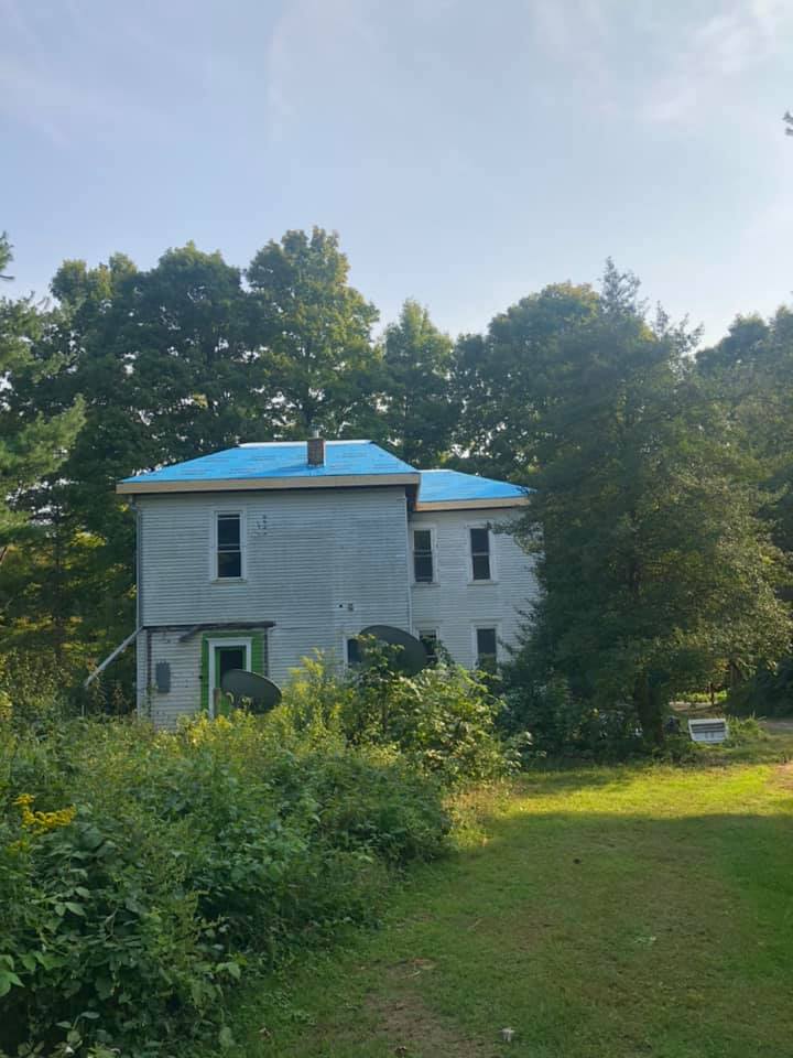 A white house with a blue roof is surrounded by trees and grass.