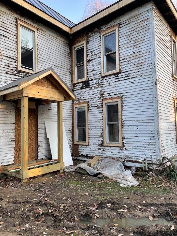 A white house with a wooden porch is being remodeled.