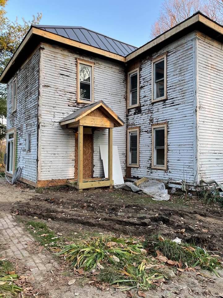 A white house with a wooden porch and a metal roof is being remodeled.
