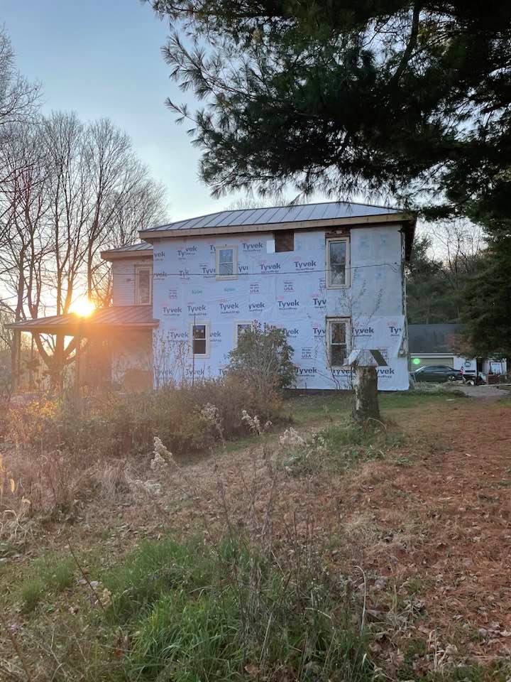 The sun is setting behind a house that is being remodeled.