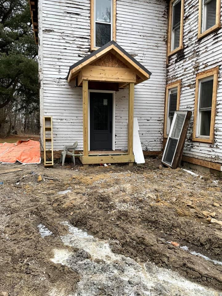 A white house with a wooden porch is being remodeled.