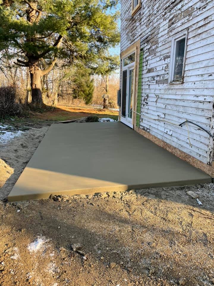 A concrete patio is being built beside a white house.