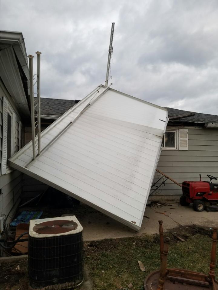A patio roof has fallen onto house from wind damage.  