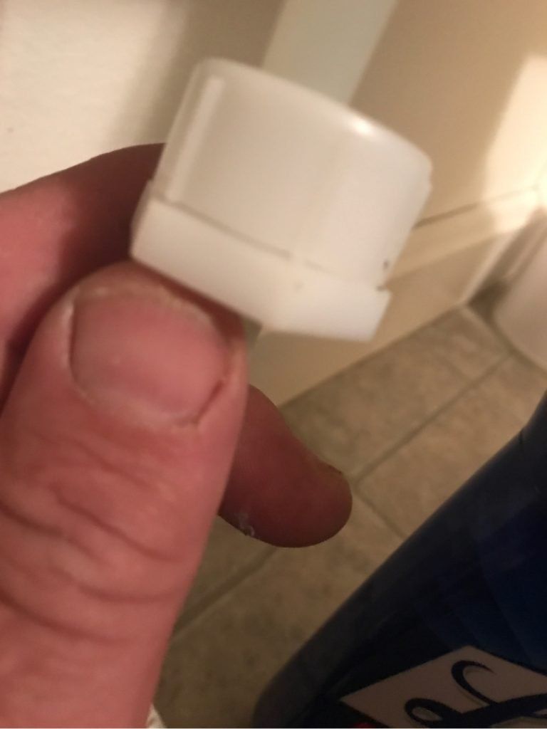 A person is holding a white plastic fitting.