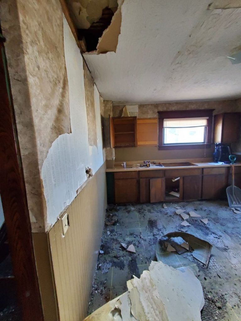 A kitchen in a water damaged house with a hole in the ceiling.