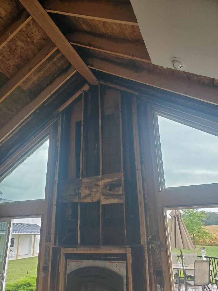 A fireplace is being repaired from fire damage in a living room with large windows.