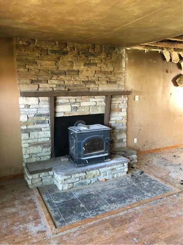 A stone fireplace with a wood stove in a living room with fire damage.