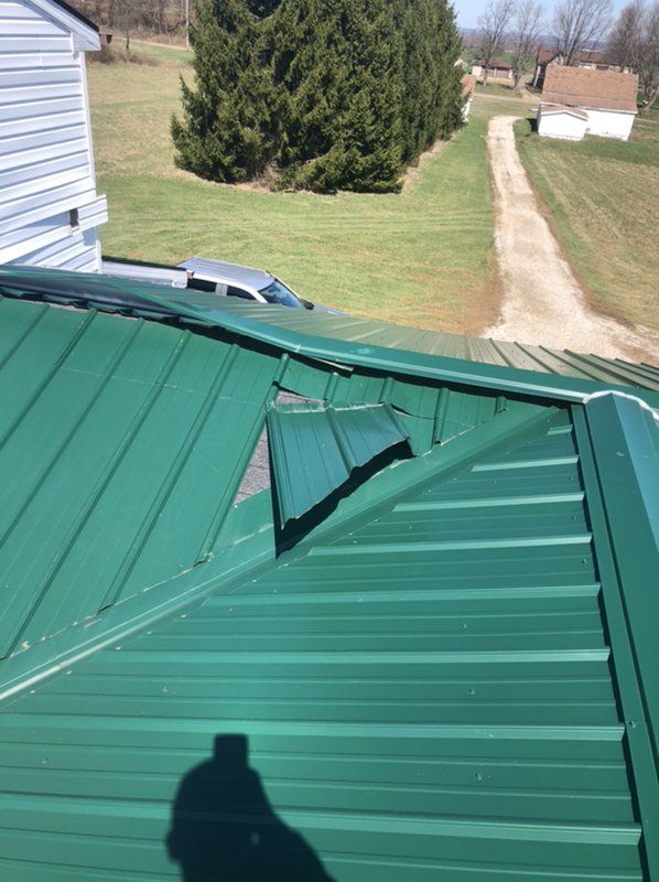 A green metal roof is sitting on top of a house with dirt driveway in background.  