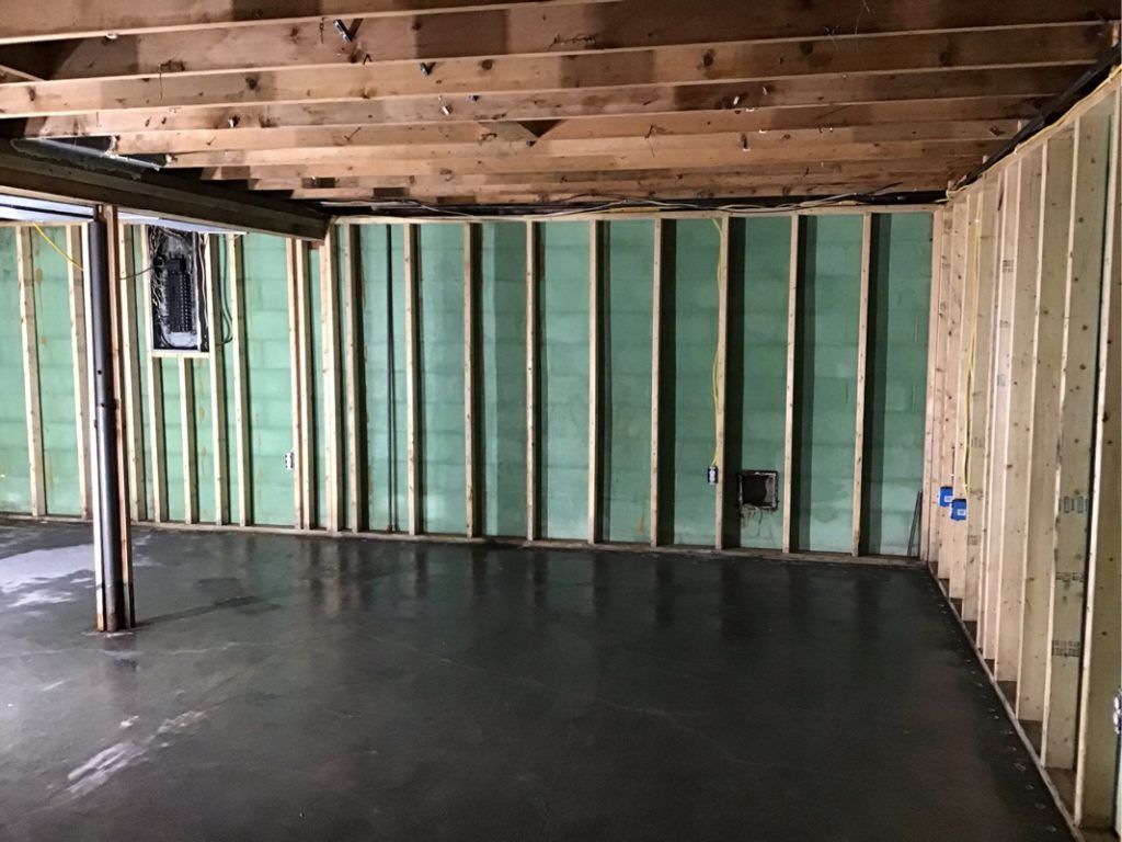 A water damaged basement under construction with a concrete floor and wooden beams.