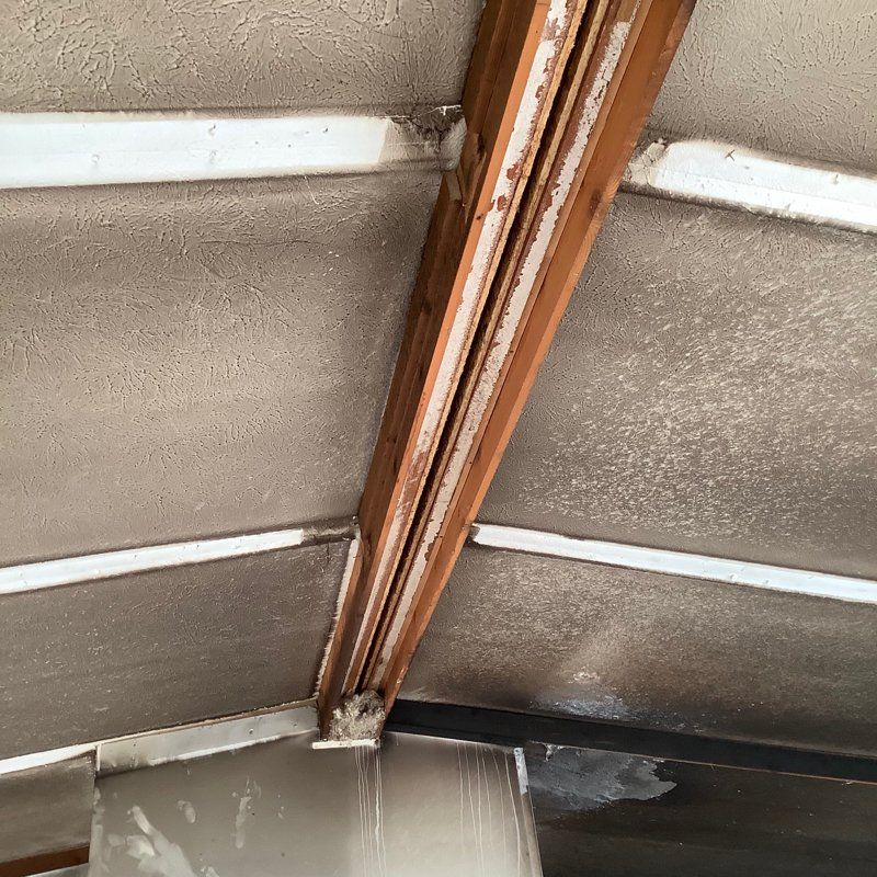 A close up of a ceiling with wooden beams which has been damaged by fire and smoke.