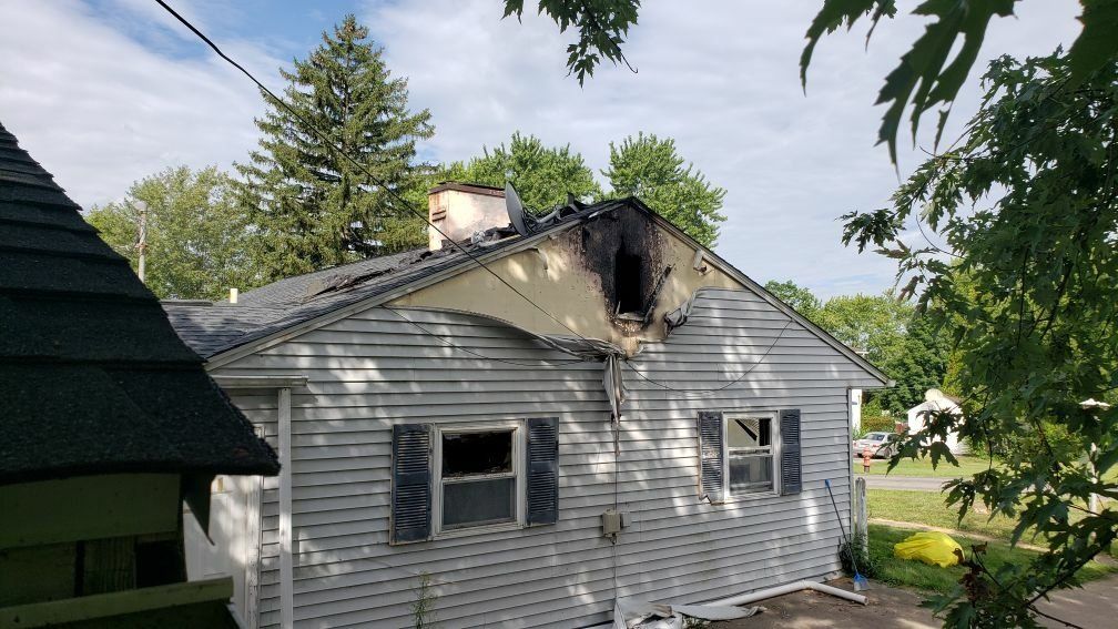 A white house with a roof that has been damaged by a fire.