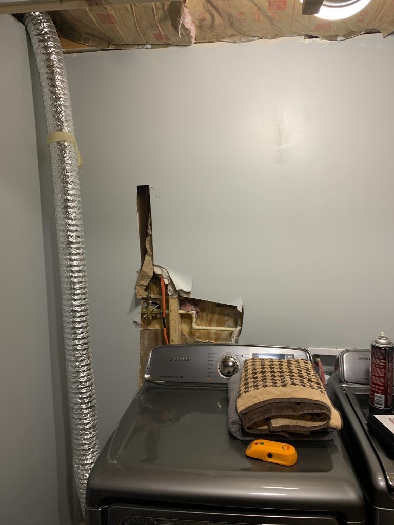 A washer and dryer in a laundry room with a hole in the wall.