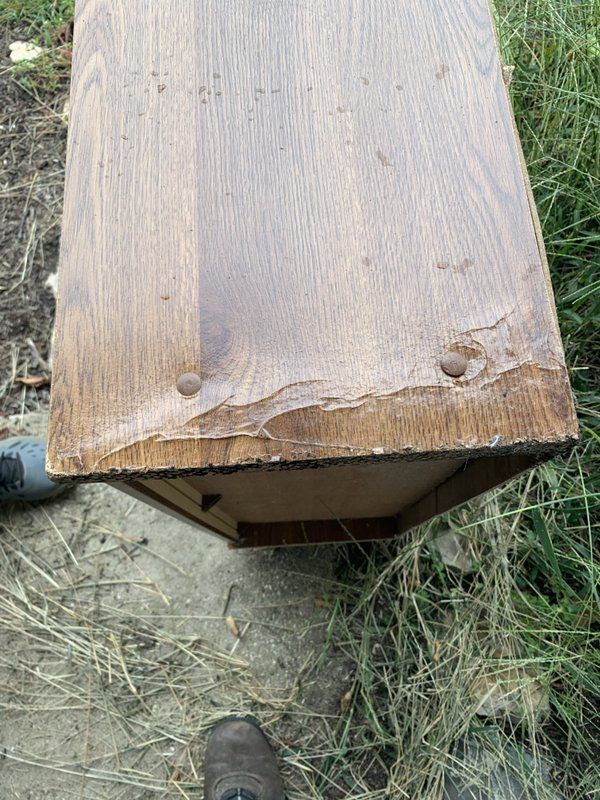 A damaged wooden table is sitting on the ground in the grass.