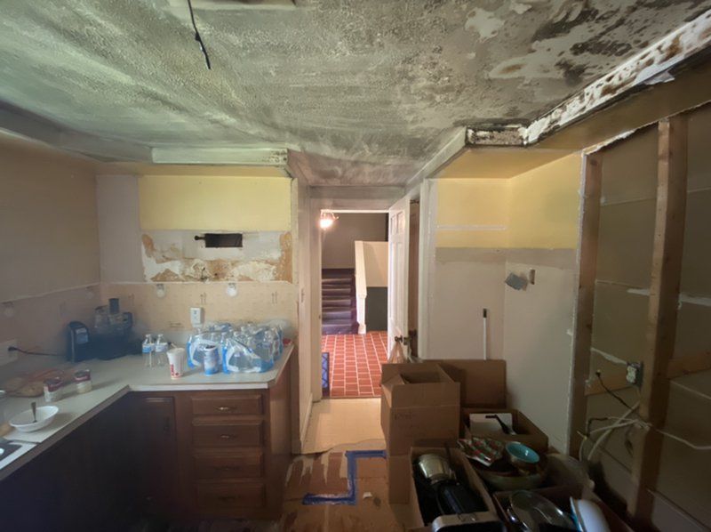 A fire damaged kitchen with boxes on the floor and a ceiling that is covered in dust.