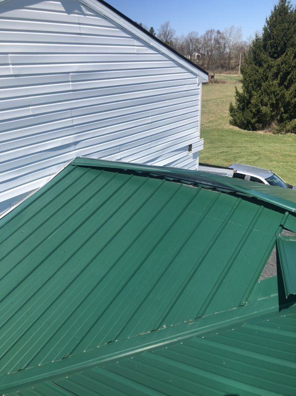 A green metal roof is sitting beside a white house.