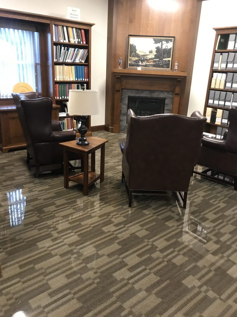A room with a fireplace, two chairs, a lamp, and carpet that is wet with flooding. 